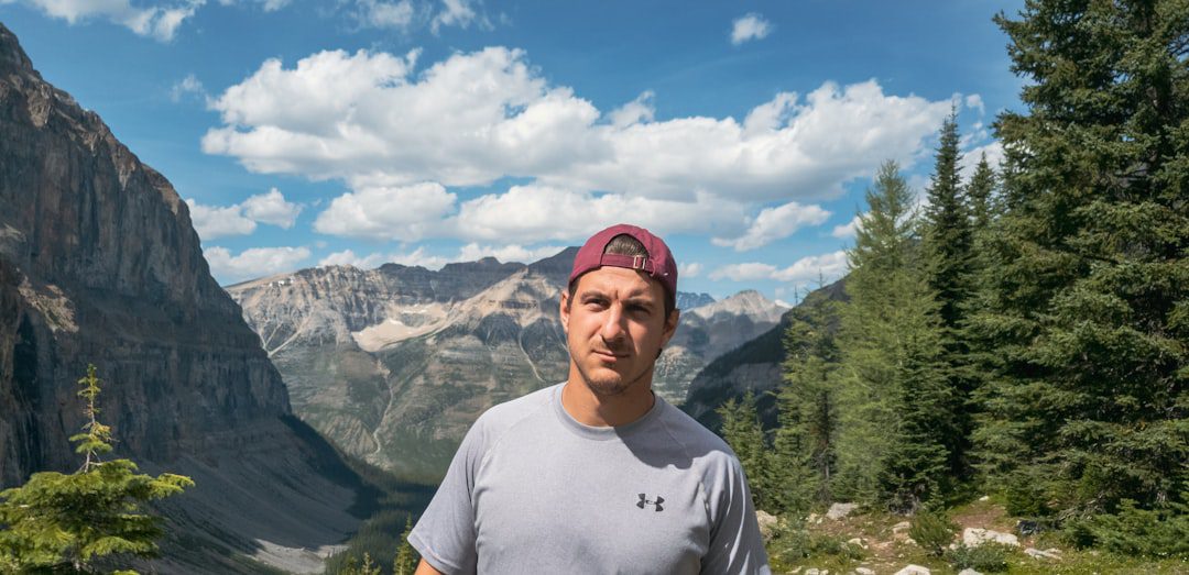 CADI certification standards. Man in white crew neck t-shirt standing near green trees and mountains during daytime