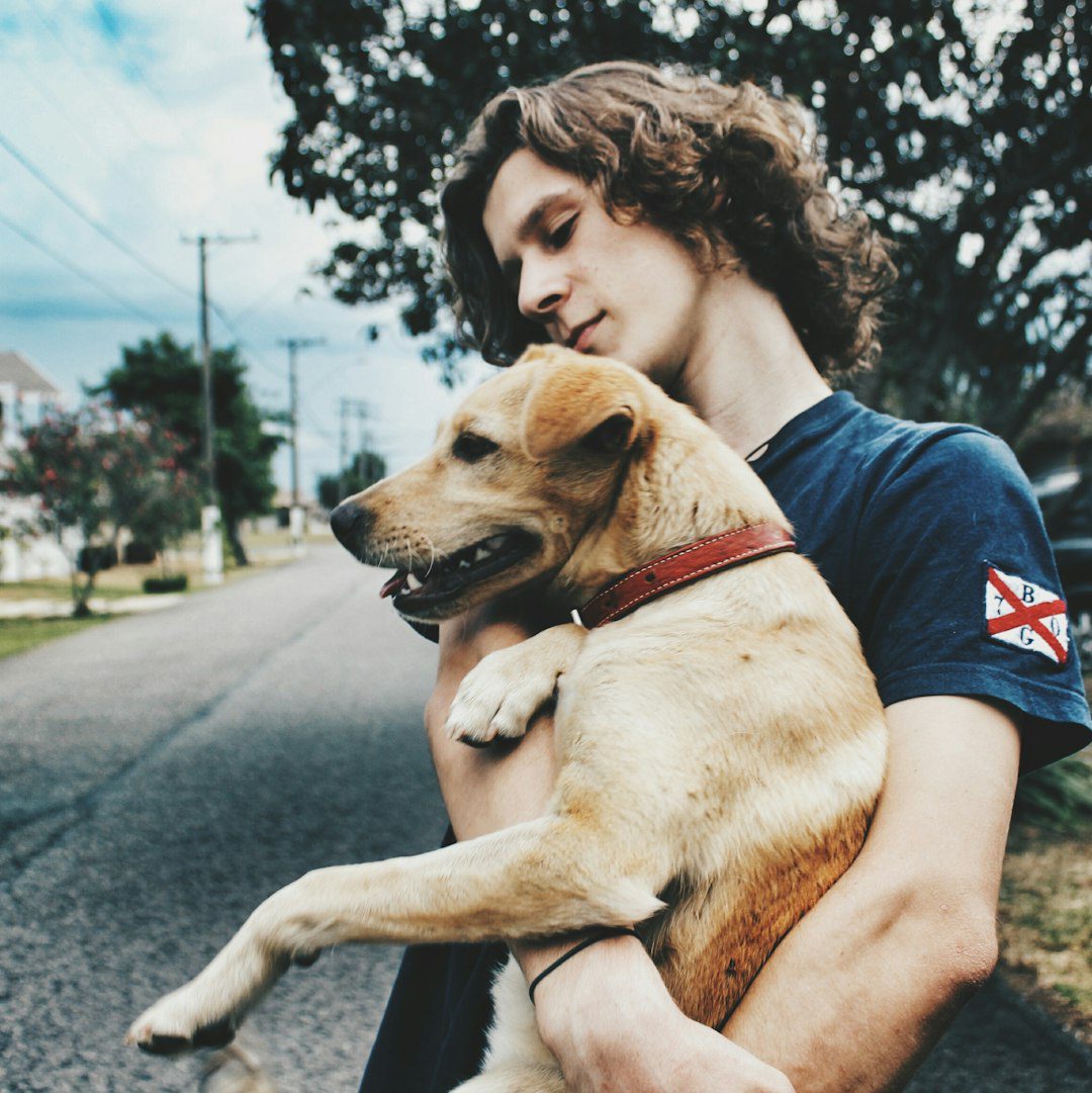 assistance dogs Canada — man in black t-shirt hugging brown short coated dog